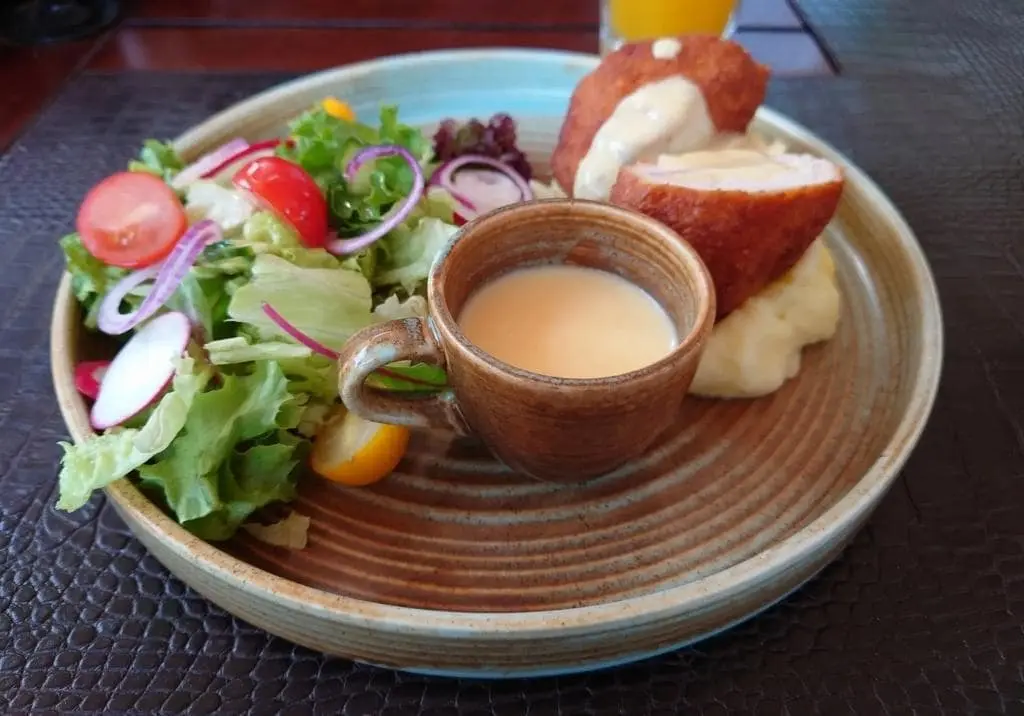 Cheese and Ham-Stuffed Chicken Breast with Crispy Coating, served on Mashed Potatoes with a Creamy Sauce and Fresh Salad